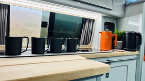 A kitchen area with a countertop, four black mugs, a kettle, and a small orange appliance. - Glen Roamer VW Campervan – Explore Scotland in Comfort & Freedom (Dunblane)
