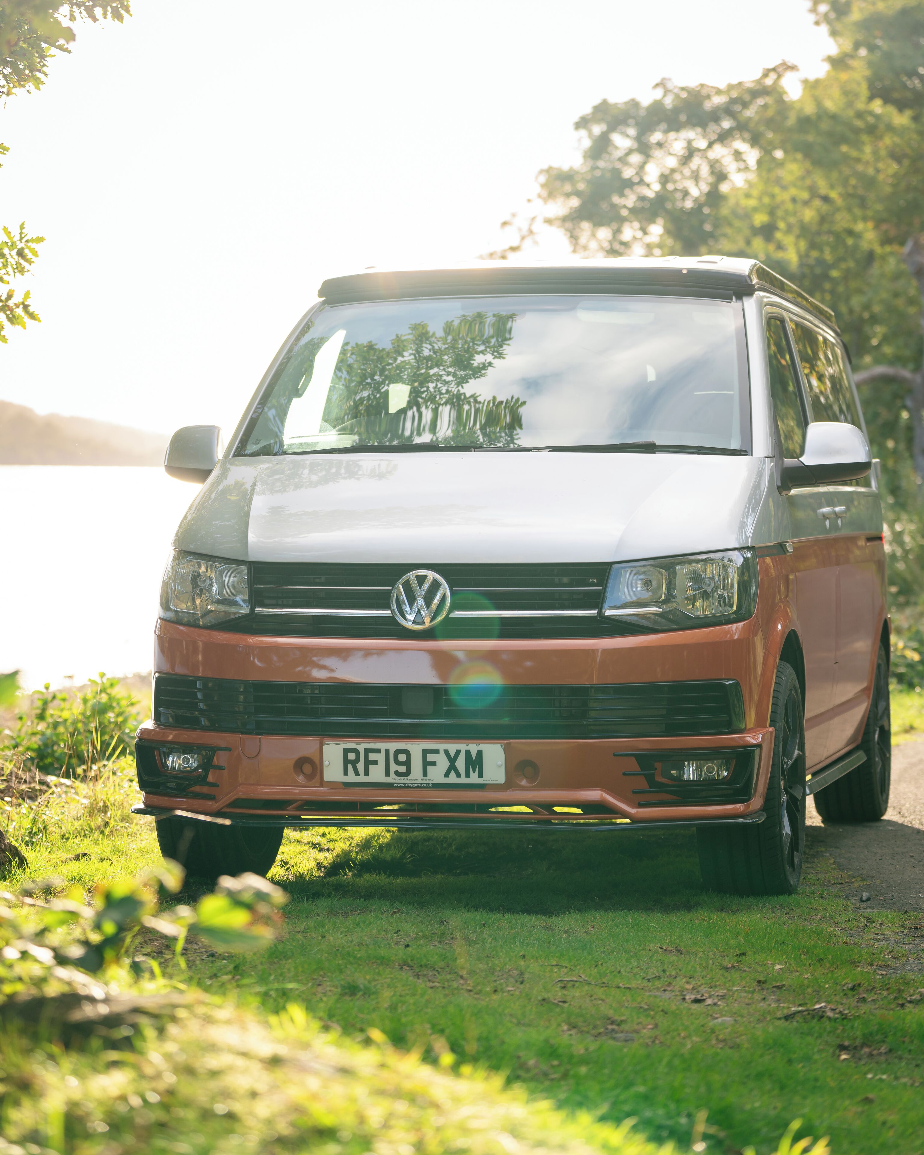 Volkswagenin pakettiauto on pysäköity ruohikkoiseen tienvarteen, ja taustalla näkyy järvi.