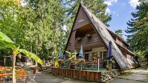 Un chalet en bois avec un toit à forte pente, entouré d’arbres et doté d’un espace salon extérieur.