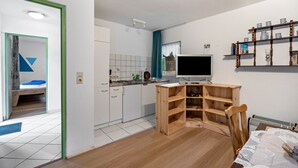 Une cuisine moderne avec des meubles blancs, une table à manger en bois et un téléviseur.