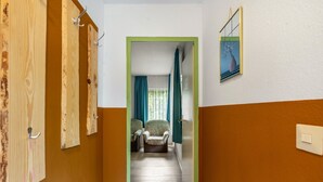 Un couloir aux murs en bois, une porte à cadre vert, une chaise et un tableau accroché au mur.