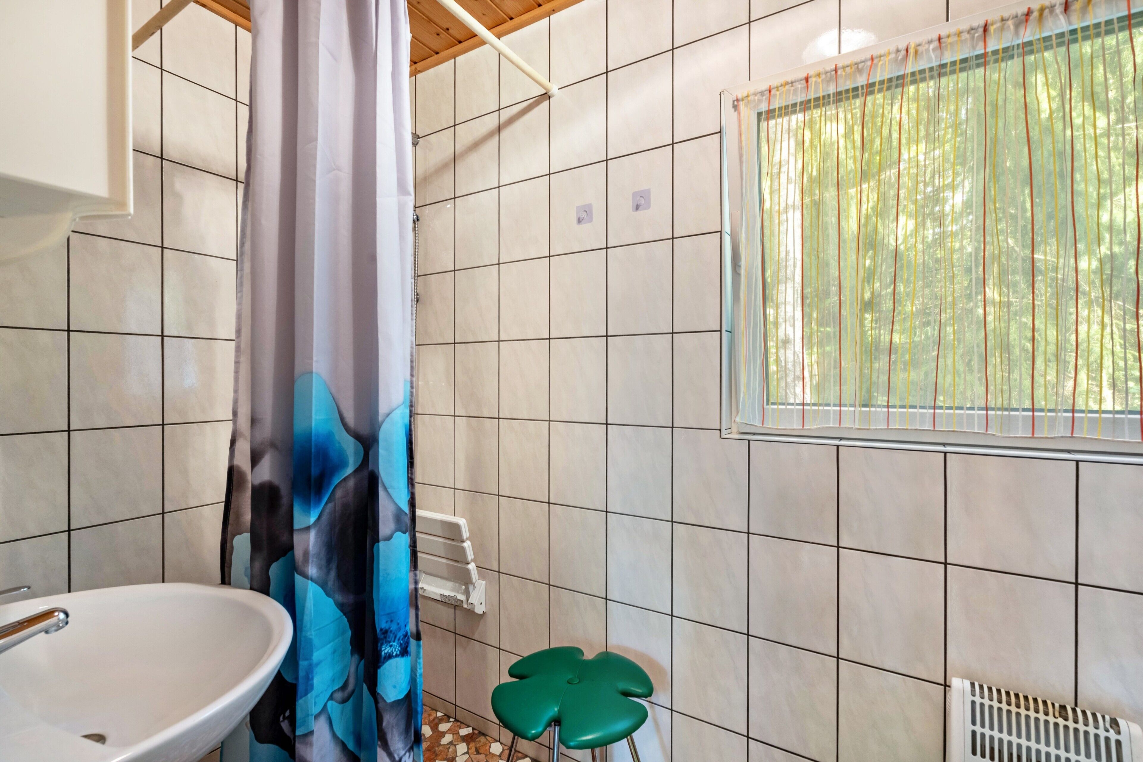 Une salle de bain équipée d’un lavabo, d’un rideau de douche, d’un radiateur et d’une fenêtre donnant sur des arbres.
