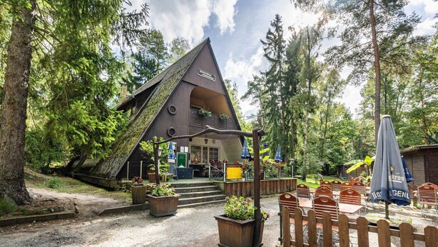 Un lodge rústico con techo triangular, mobiliario exterior y cerca de madera.