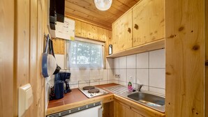 A compact kitchen with wooden cabinets, a small refrigerator, a sink, and a window with a view of trees. - Bungalow '1 - Kimbucht' with Private Terrace and Shared Garden (Waldhufen)