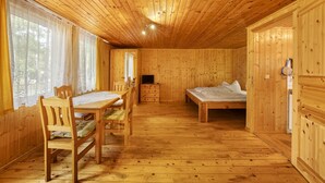 A wooden cabin interior with a dining table, chairs, a bed, and a television. - Bungalow '1 - Kimbucht' with Private Terrace and Shared Garden (Waldhufen)