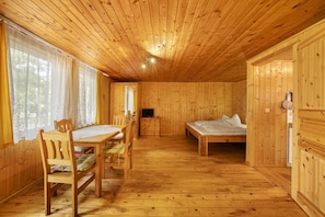 A wooden cabin interior with a dining table, chairs, a bed, and a television.