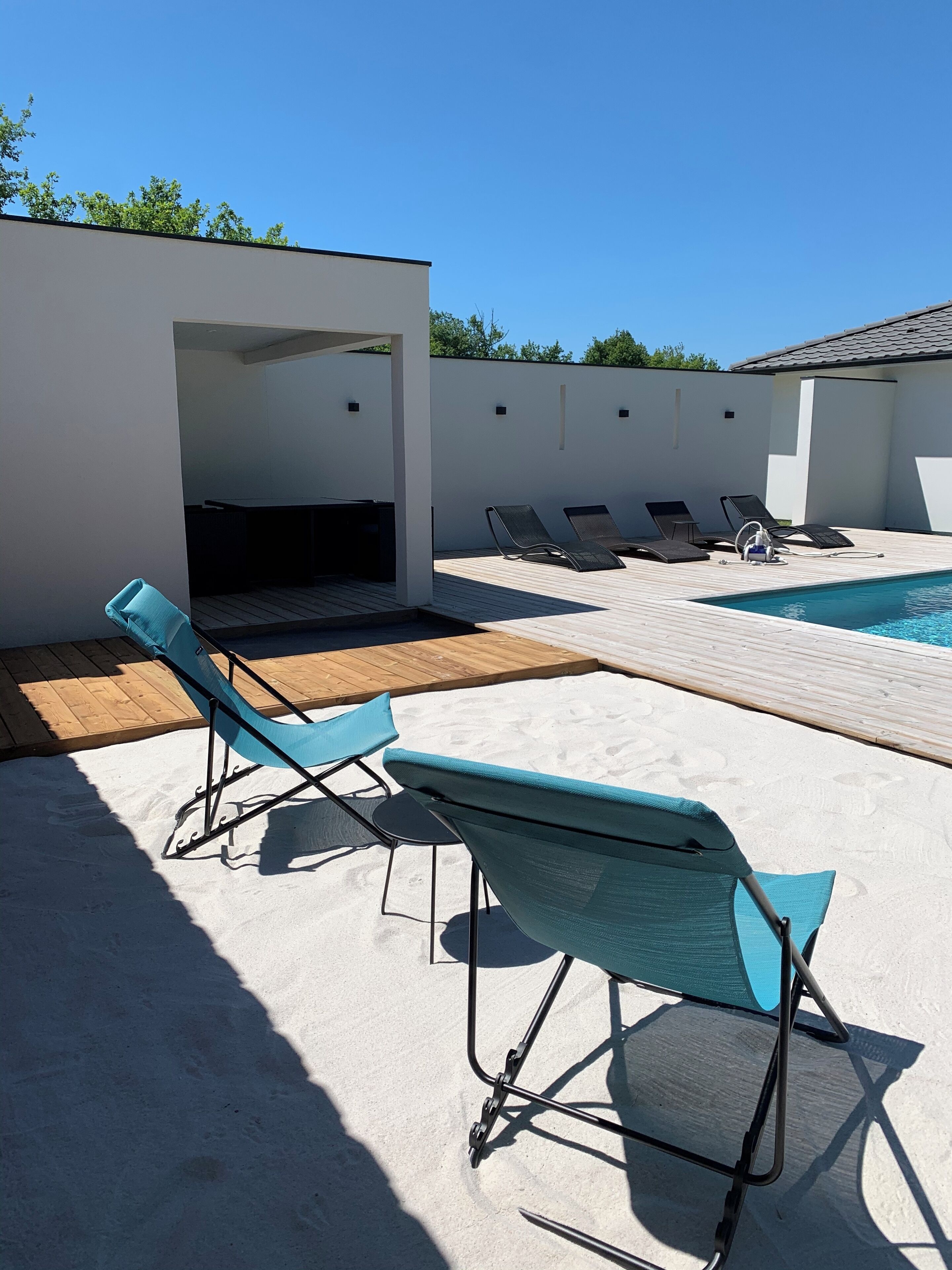 Un área de piscina moderna al aire libre con sillones de descanso y una terraza de madera.