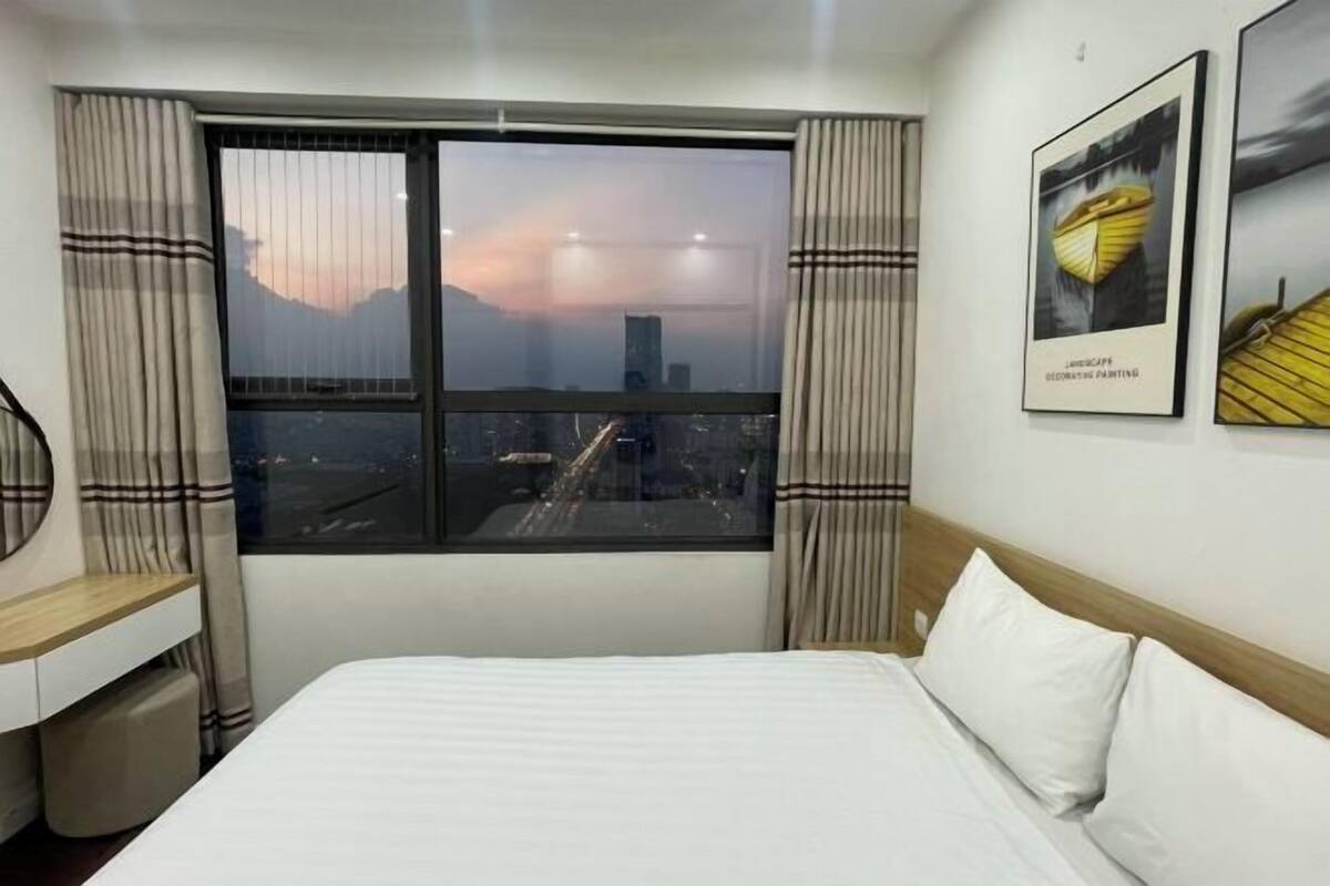 Ein Hotelzimmer mit einem Bett, einem Schreibtisch, einem Fenster mit Vorhängen und Blick auf die Stadt.