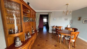 Un coin repas avec une table et des chaises en bois, un buffet contenant de la verrerie, et un couloir menant à une autre pièce.