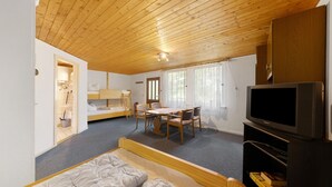 Una habitación con techo de madera, una cama, un televisor, una mesa de comedor con sillas y una pequeña zona de kitchenette.