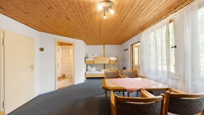 Una habitación con una cama individual superpuesta, una mesa de comedor con sillas, una lámpara en el techo y una ventana con cortinas.