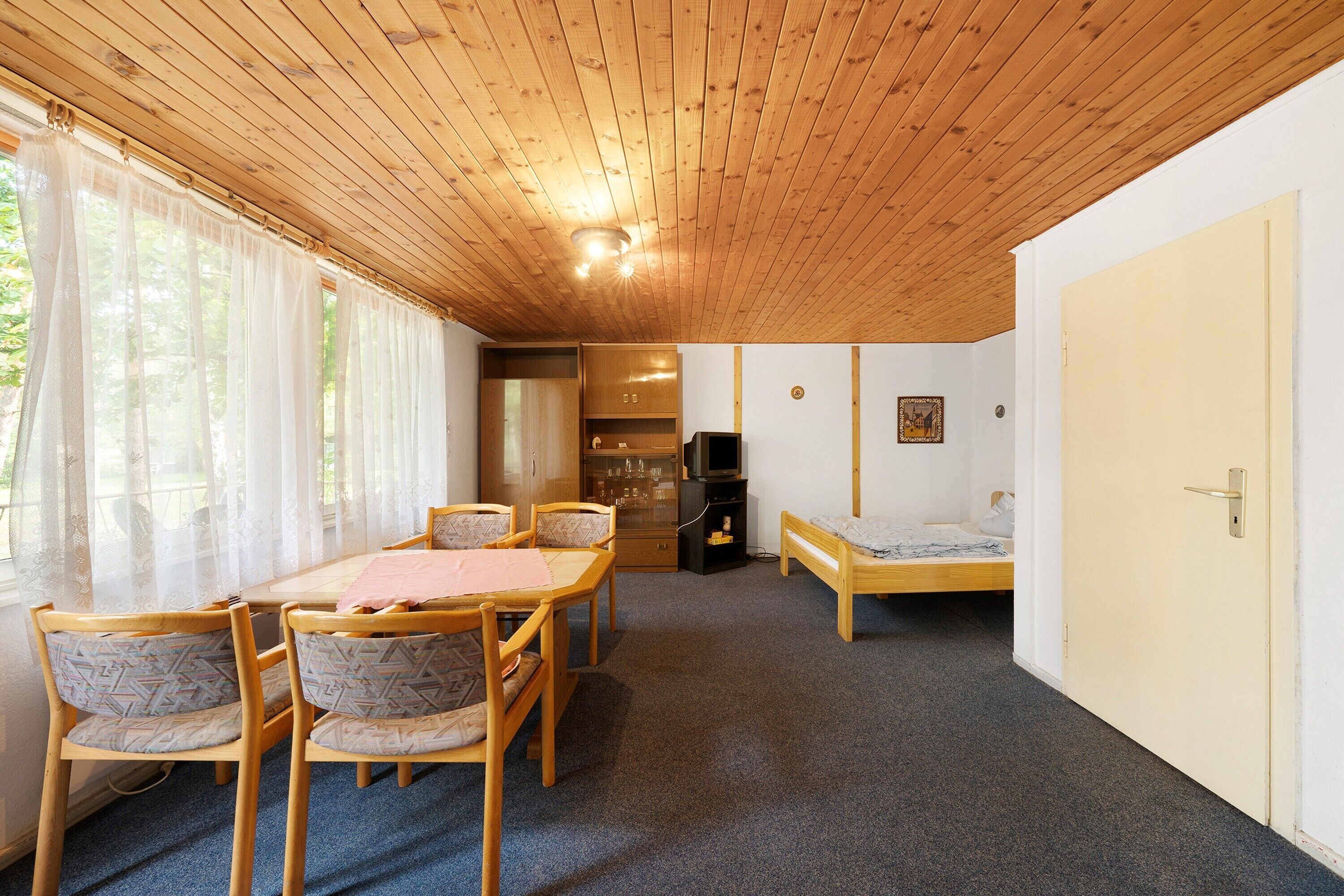 Une pièce avec un plafond en bois, une table à manger avec des chaises, un lit, un téléviseur et une porte.