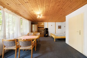 A room with a wooden ceiling, a dining table with chairs, a bed, a television, and a door.