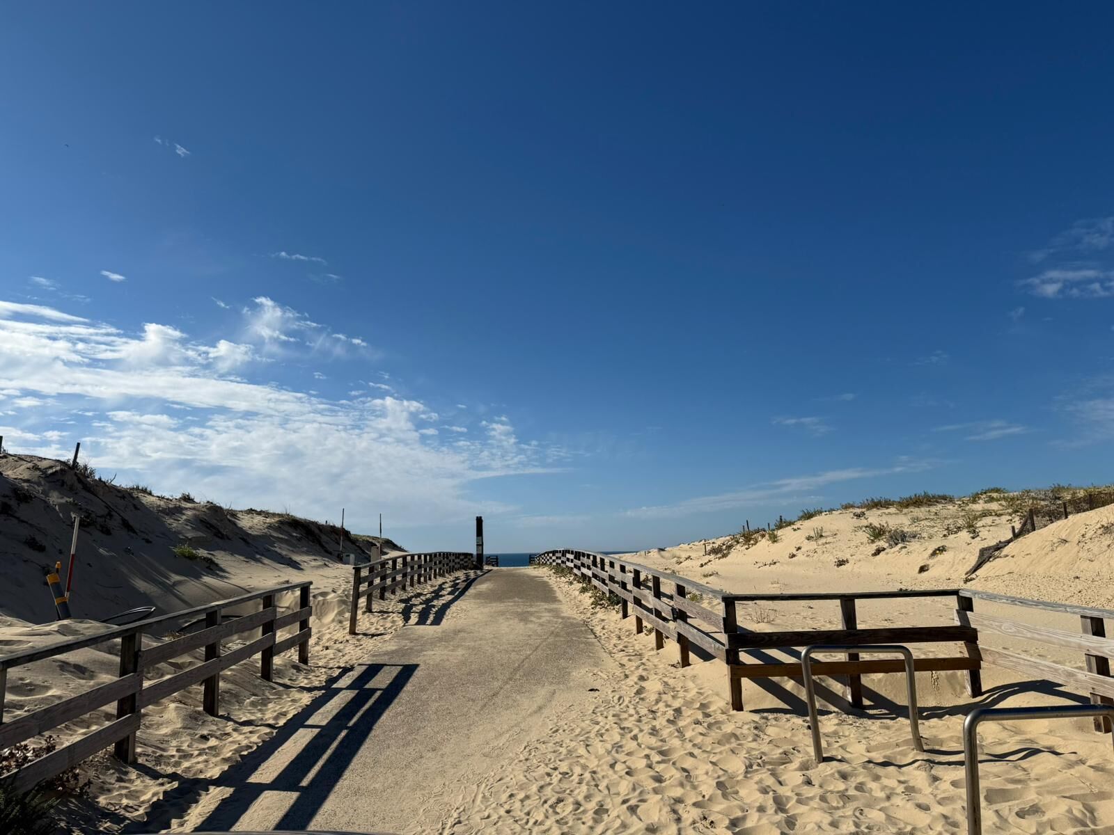 A sandy beach path with wooden railings and a clear sky.