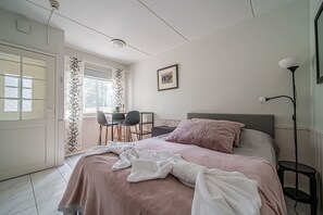 Ein Schlafzimmer mit Bett, Schreibtisch, Stühlen, einer Lampe und einem Fenster.