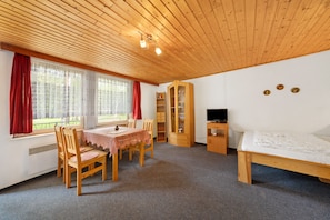 Une pièce avec un plafond en bois, une table à manger avec des chaises, un lit, un téléviseur et une bibliothèque.
