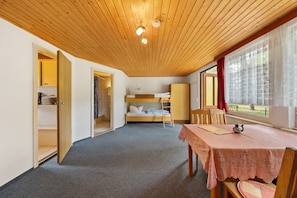 Une chambre avec un lit superposé, un plafond en bois, une table recouverte d’une nappe en dentelle et une fenêtre avec des rideaux.