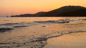 A beach at sunset with waves and a sailboat in the distance. - Domus Sole (Campulongu)