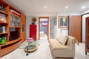 Una sala de estar con sofá, televisor, estantería y una mesa de centro de vidrio.