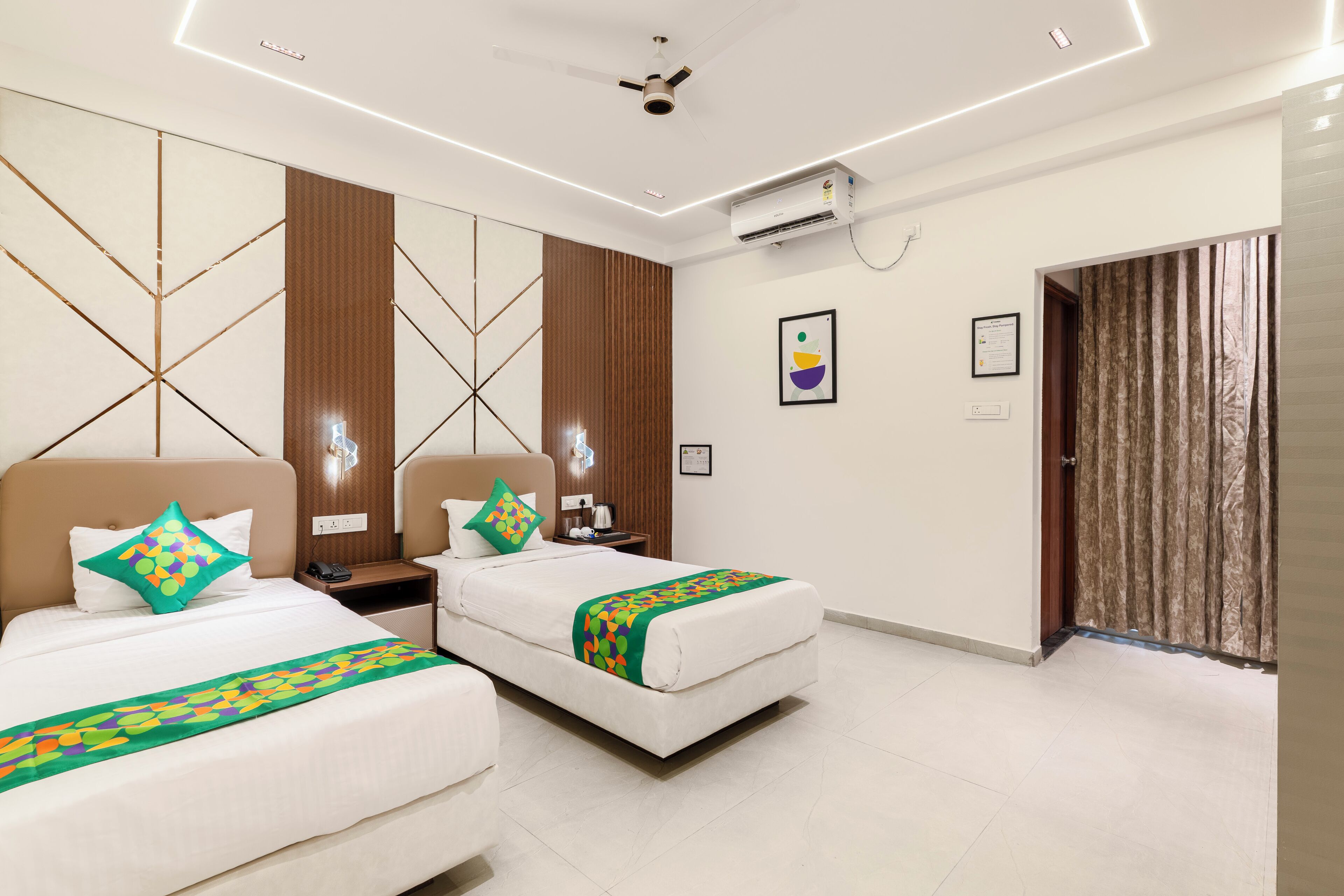 A hotel room with two beds, a ceiling fan, an air conditioning unit, a wooden panel wall, and a door with curtains.