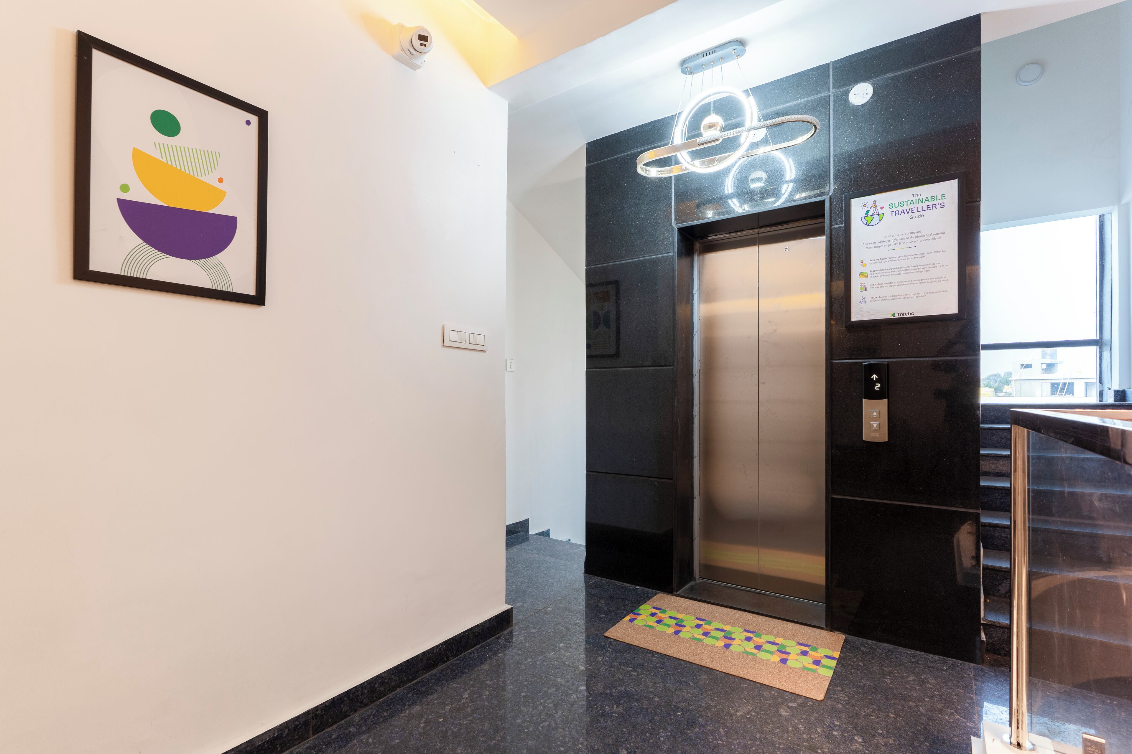 A modern elevator with a digital display, a framed abstract artwork on the wall, and a sign indicating a sustainable travel initiative.