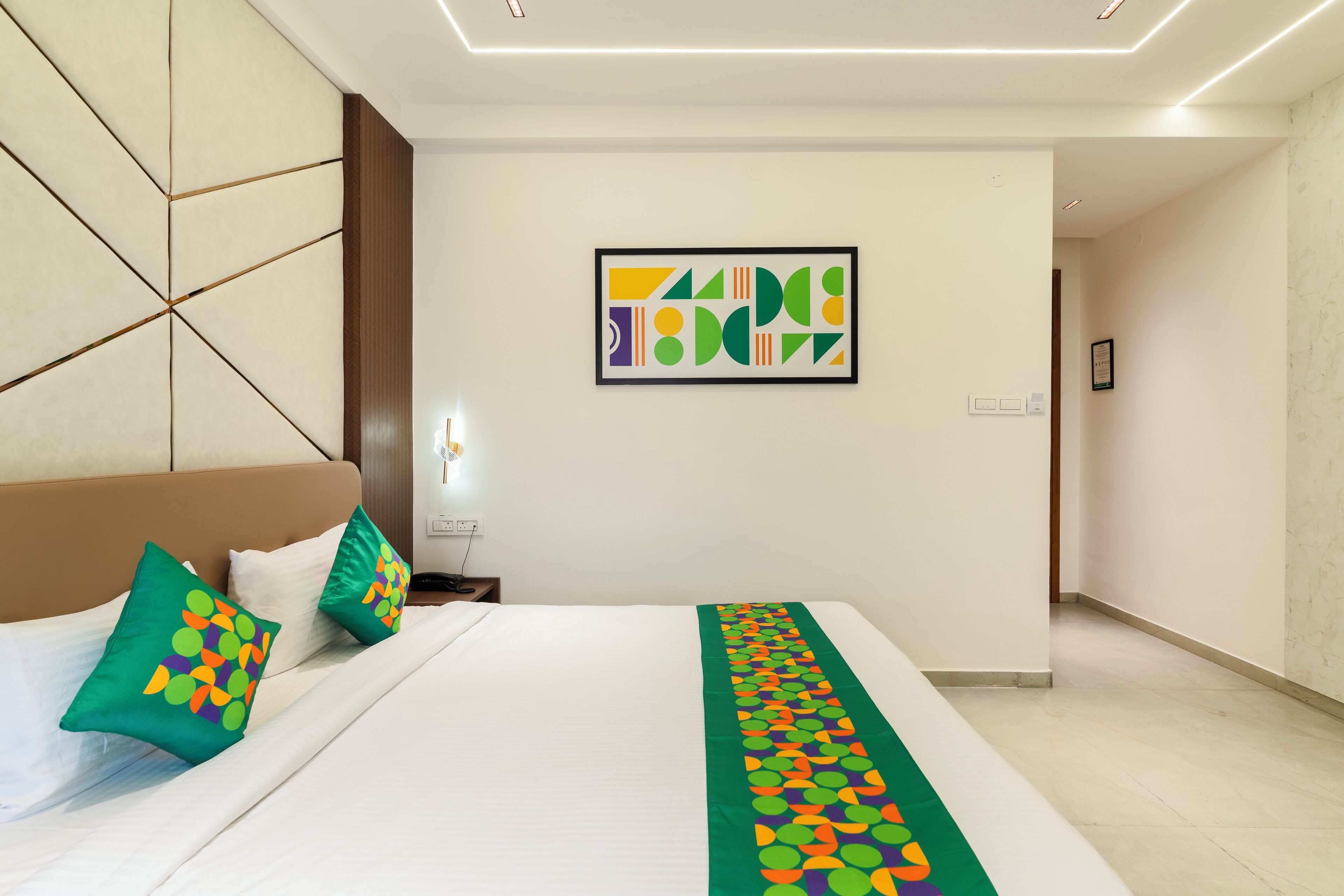 Una habitación de hotel moderna con una cama grande, un cabecero, una obra de arte abstracta colgada en la pared y un pasillo que conduce a otra habitación.