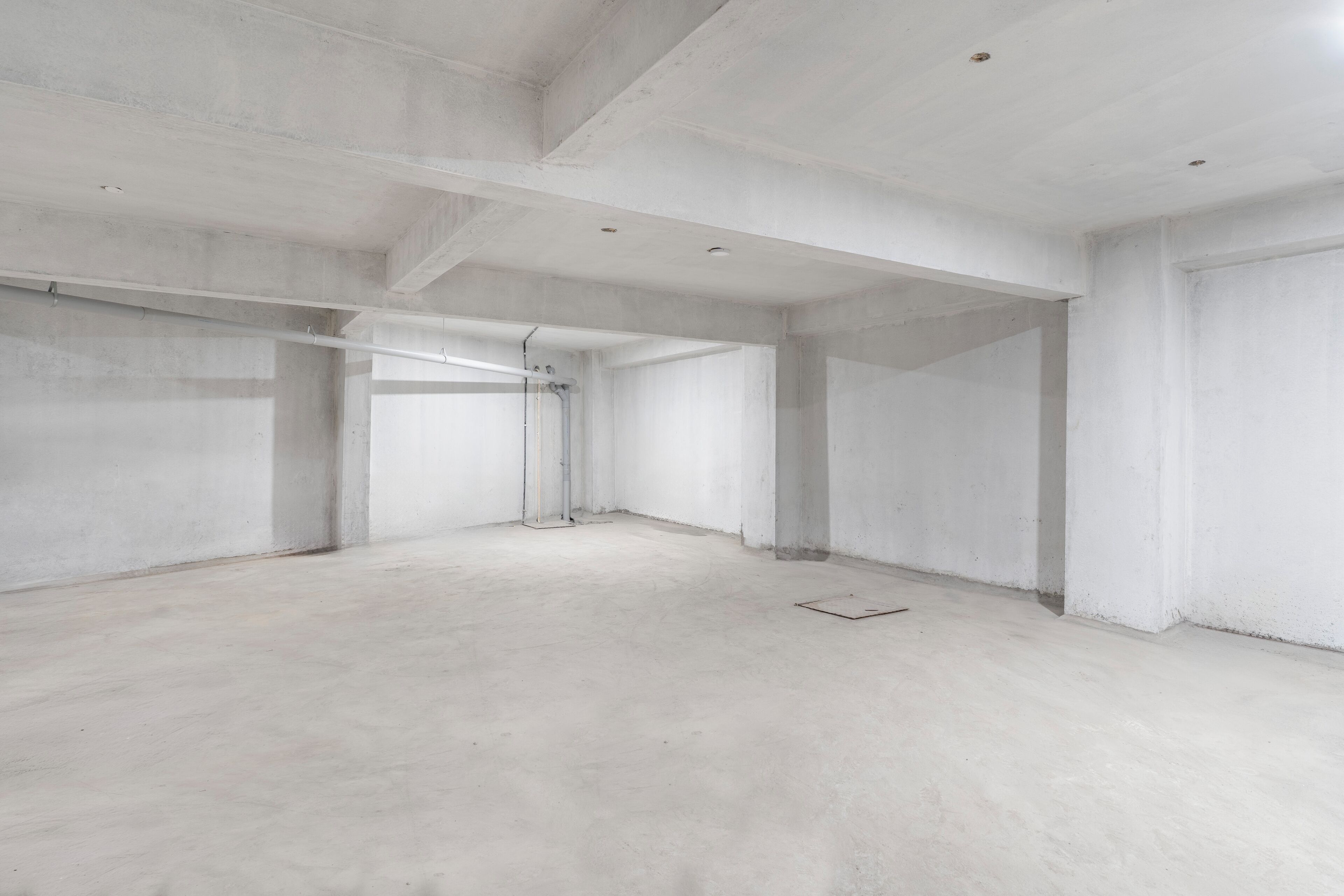 A spacious, unfinished interior with concrete walls and floors, visible structural beams, and a central corridor.