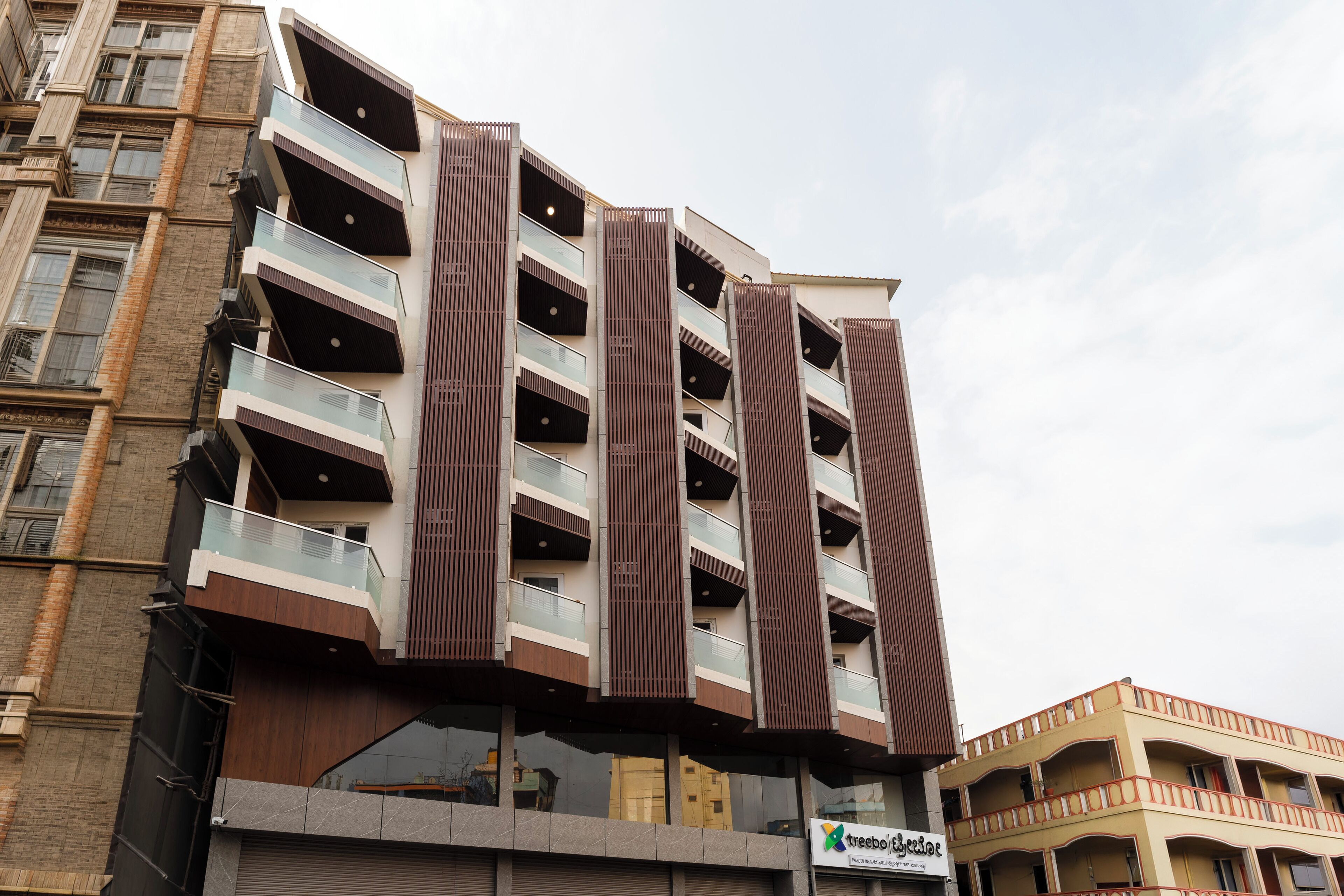 Un edificio de varios pisos con balcones, un cartel que dice 'treebo Beach Resort' visible, y una mezcla de estilos arquitectónicos modernos y tradicionales.
