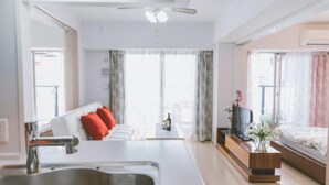 A modern living room with a sofa, a TV, a wooden side table, and a large window. - Hema Homestay Nihonbashi (Osaka)