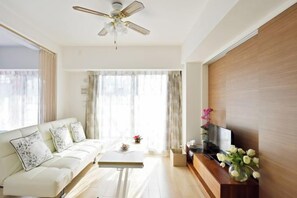 Een moderne woonkamer met een bank, salontafel, televisie en decoratieve bloemen.