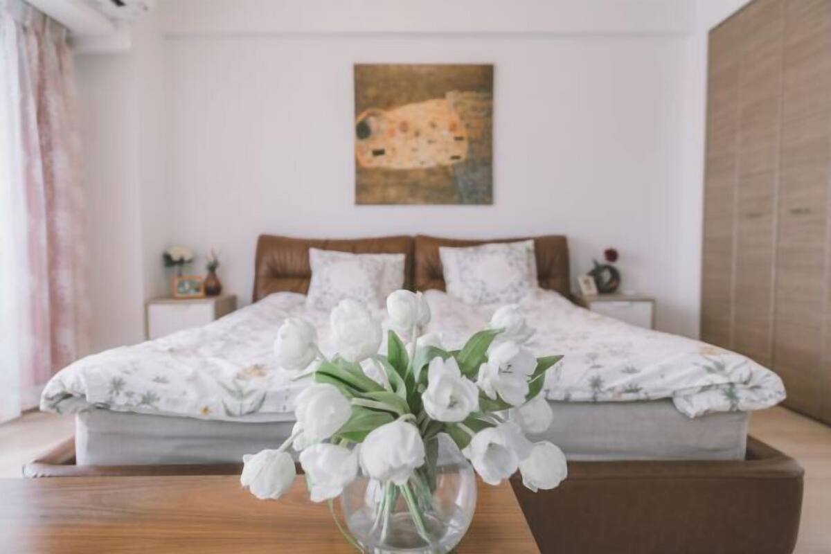 Ein Schlafzimmer mit einem Bett, einer Blumenvase mit weißen Blumen und einem Bild an der Wand.