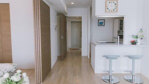 A modern kitchen with a central island and two bar stools, a wooden door, and a hallway leading to another room. - Hema Homestay Nihonbashi (Osaka)