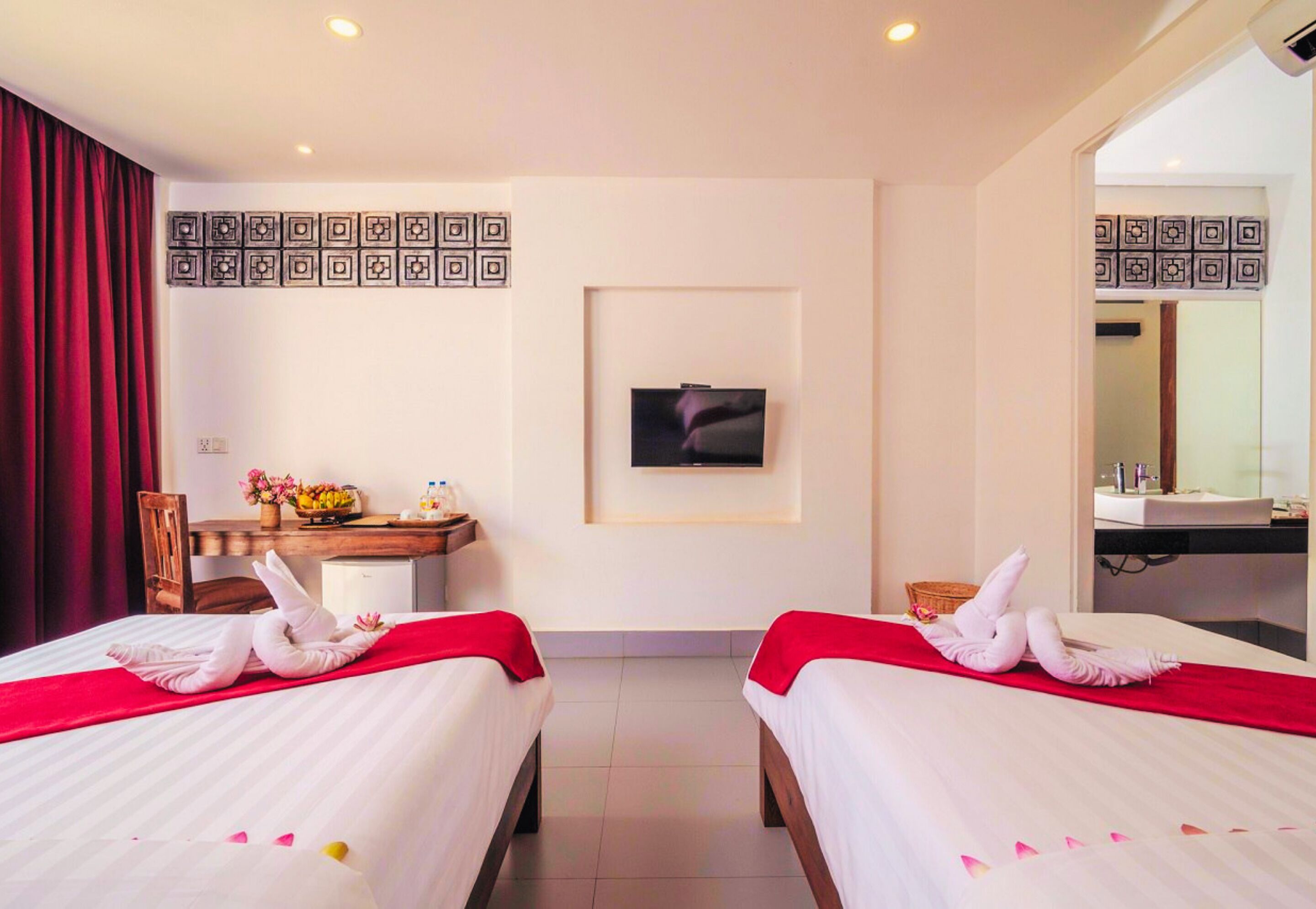 Habitación de hotel con dos camas, televisión, escritorio con silla, espejo y cortina roja.