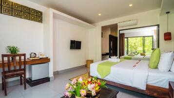 A hotel room with a bed, a desk with a chair, a small refrigerator, a television, and a window with a view of greenery.