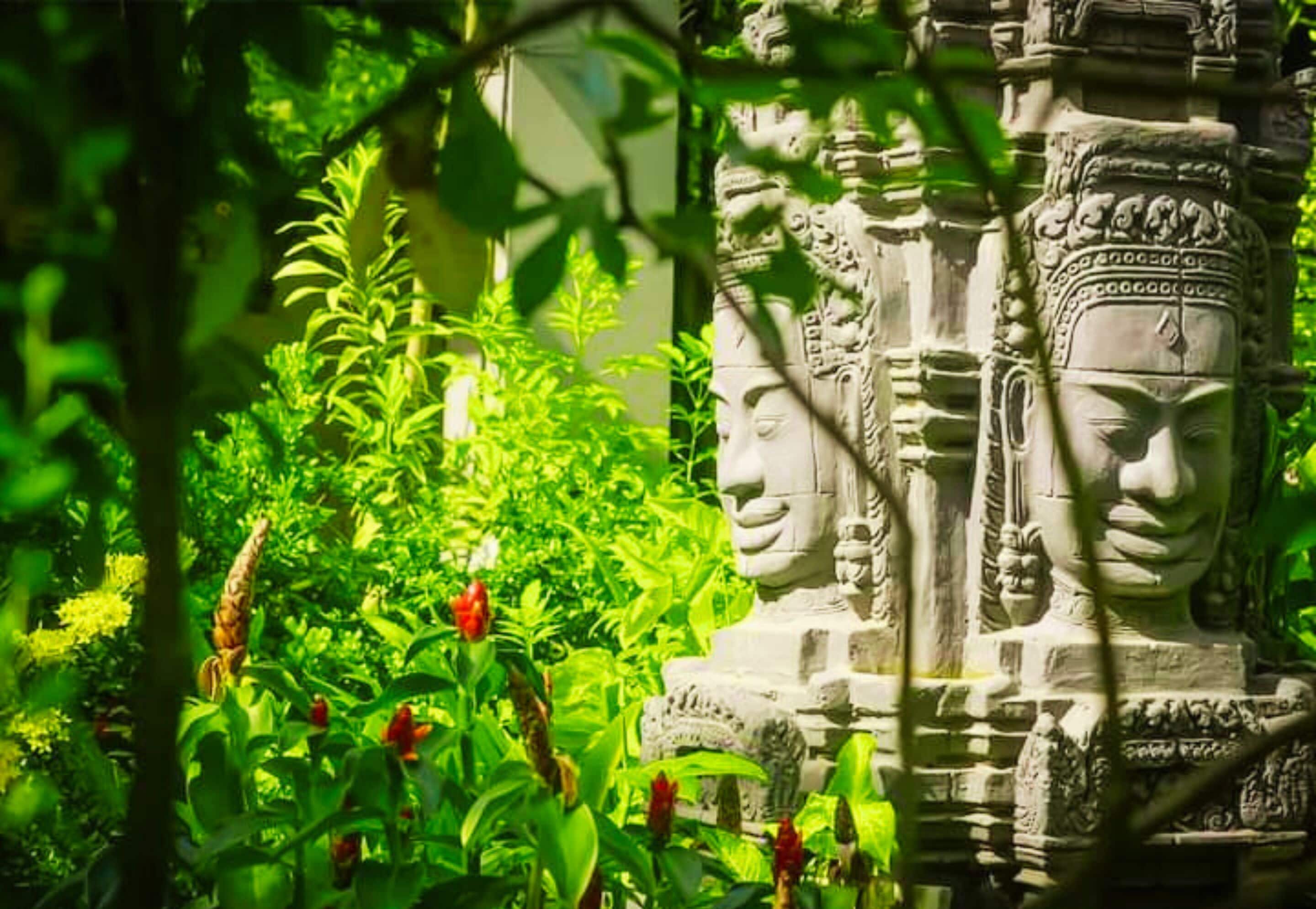 A stone structure with intricate carvings, surrounded by lush greenery and red flowers.
