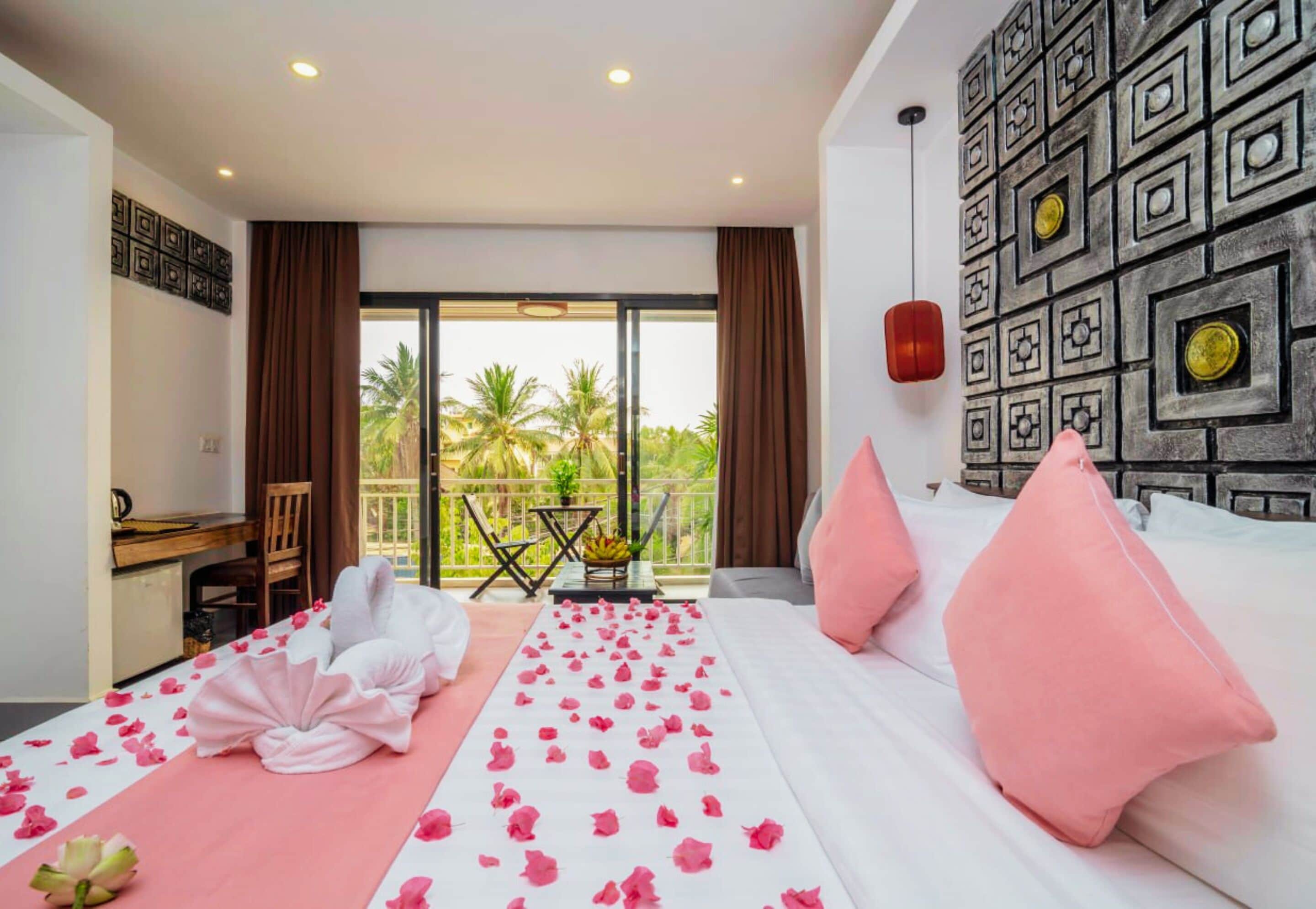A hotel room with a bed, a desk, and a balcony with a view of palm trees.
