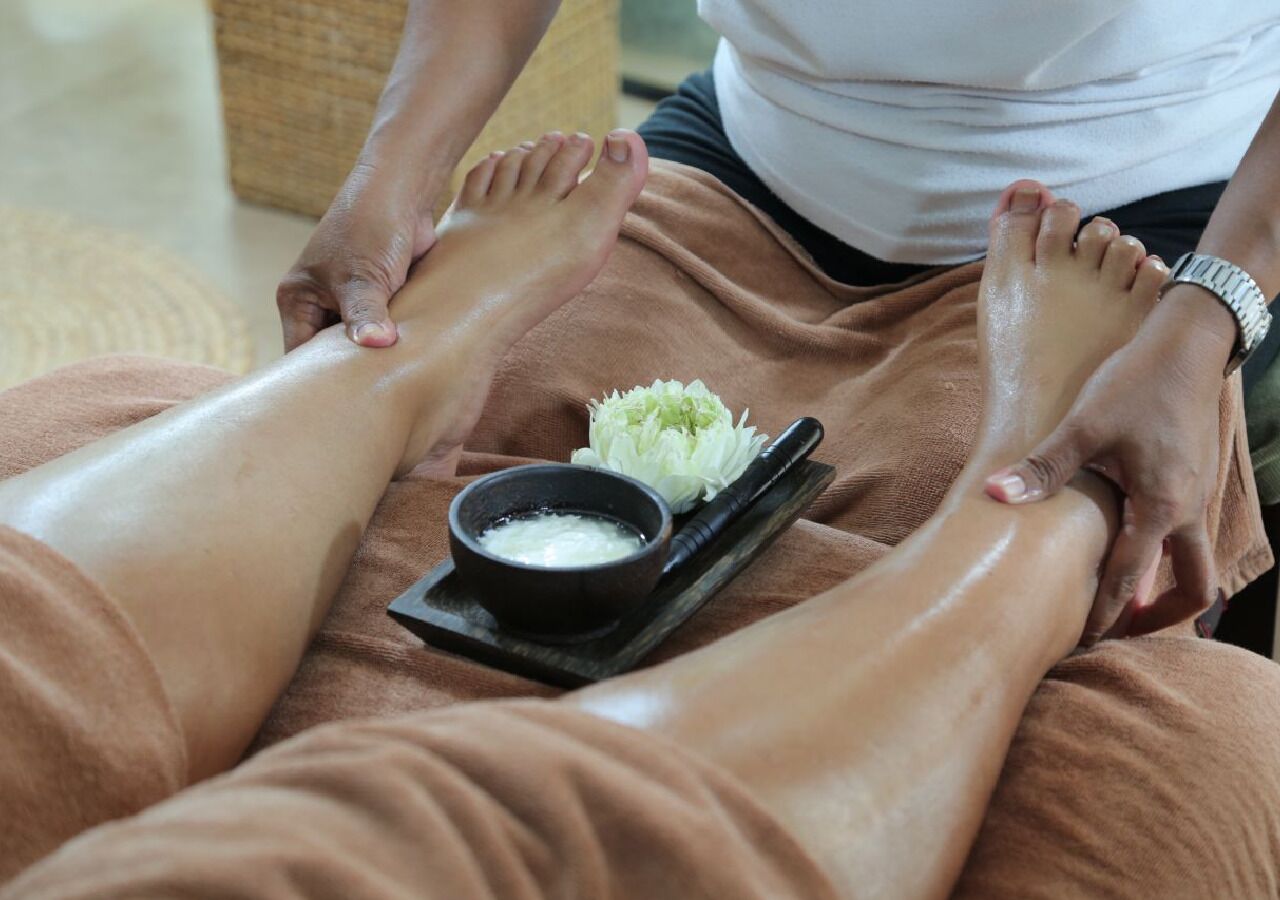 A person receiving a foot massage with a bowl of white substance and a flower on a tray.