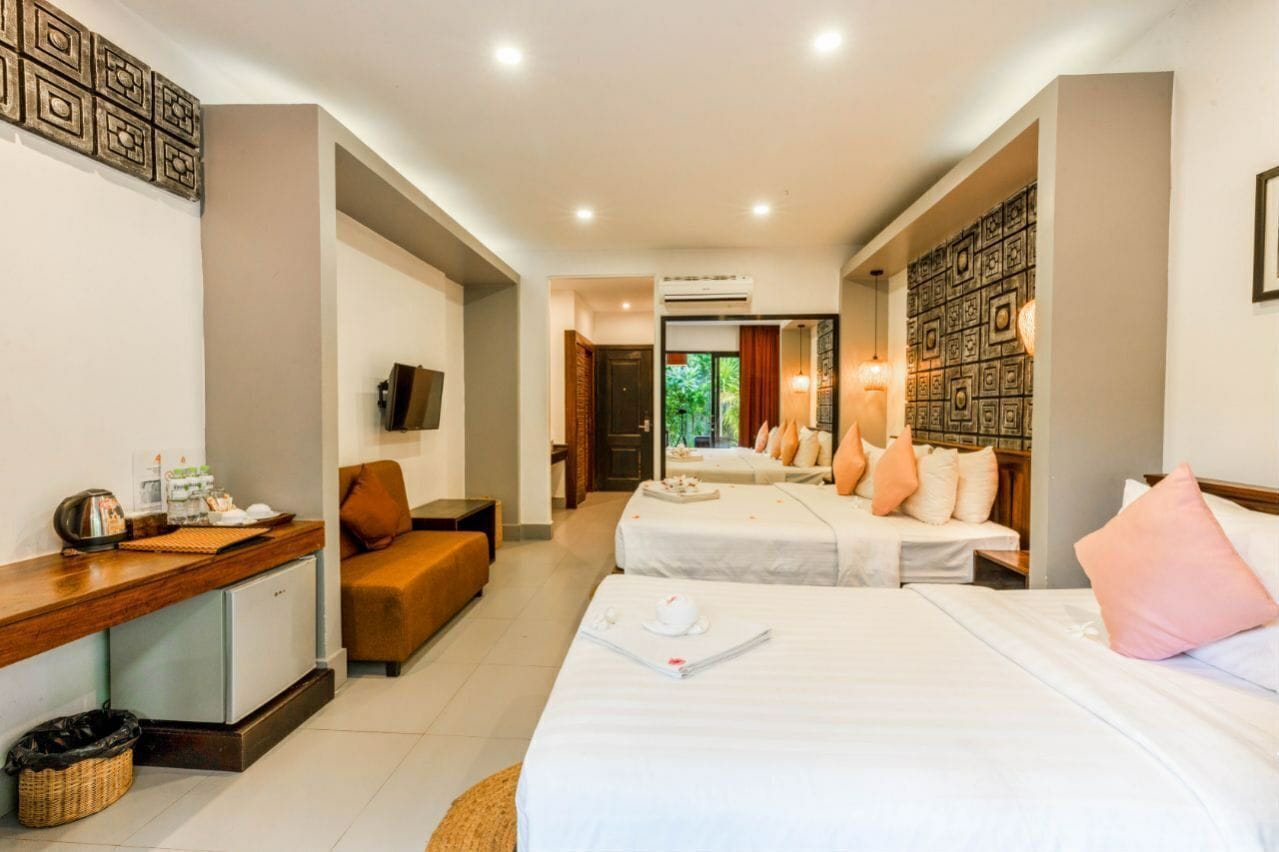 A hotel room with two beds, a desk, a TV, and a view of the outdoors.