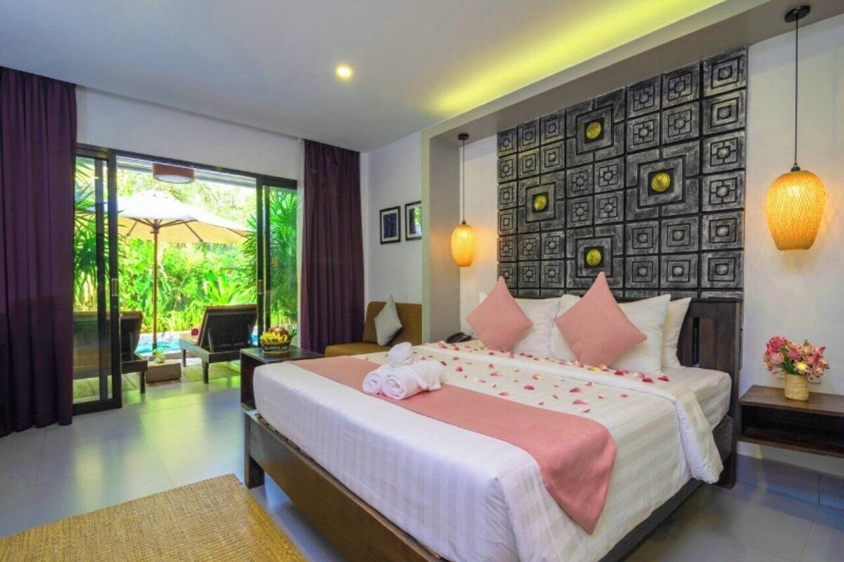 A hotel room with a large bed, a view of a pool, and a balcony with a table and chairs.