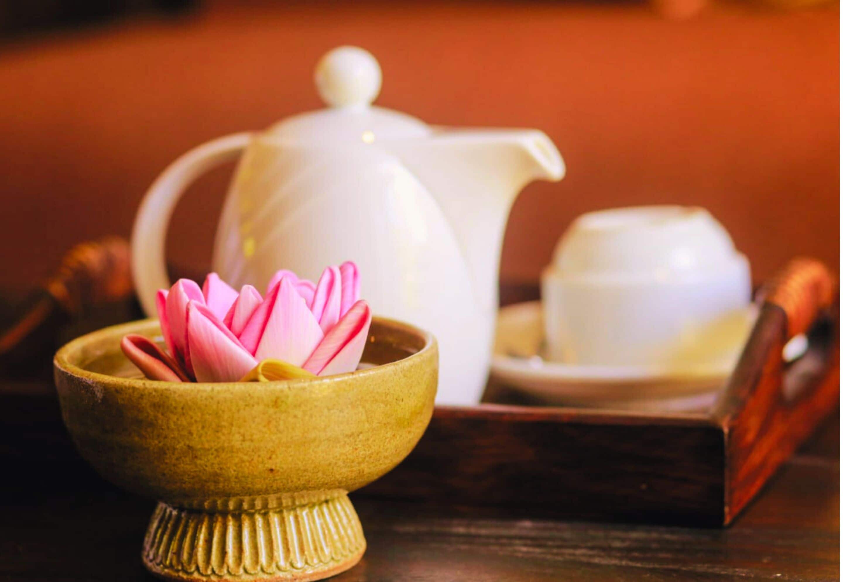 A traditional tea set with a teapot, a cup, and a small bowl containing a pink lotus flower.