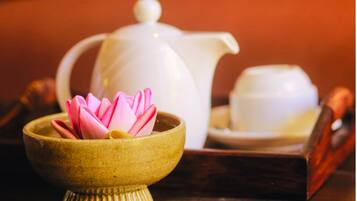 A traditional tea set with a teapot, a cup, and a small bowl containing a pink lotus flower.