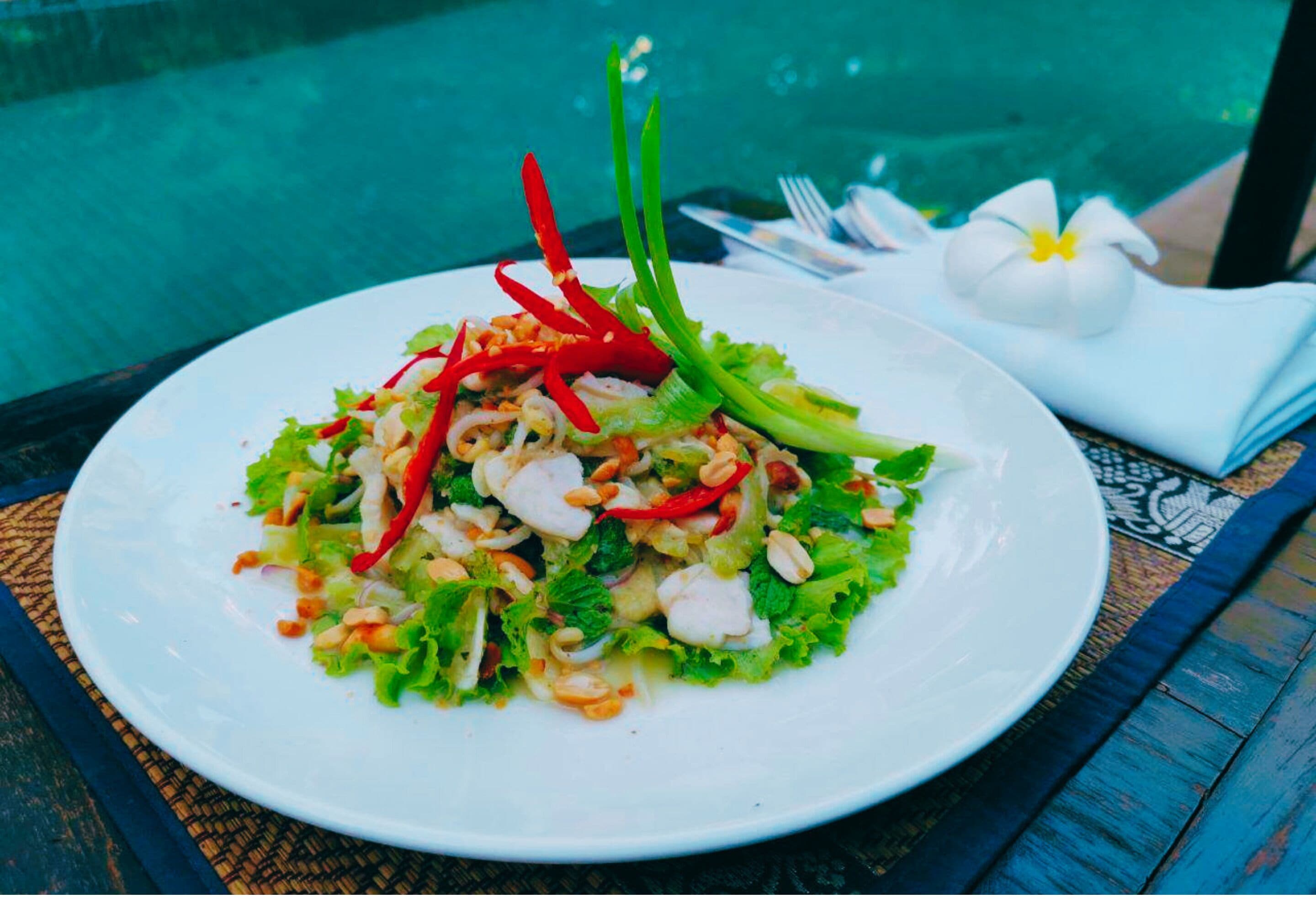 A plate of salad with red chili and green garnish, placed on a table with a blue and white patterned tablecloth.