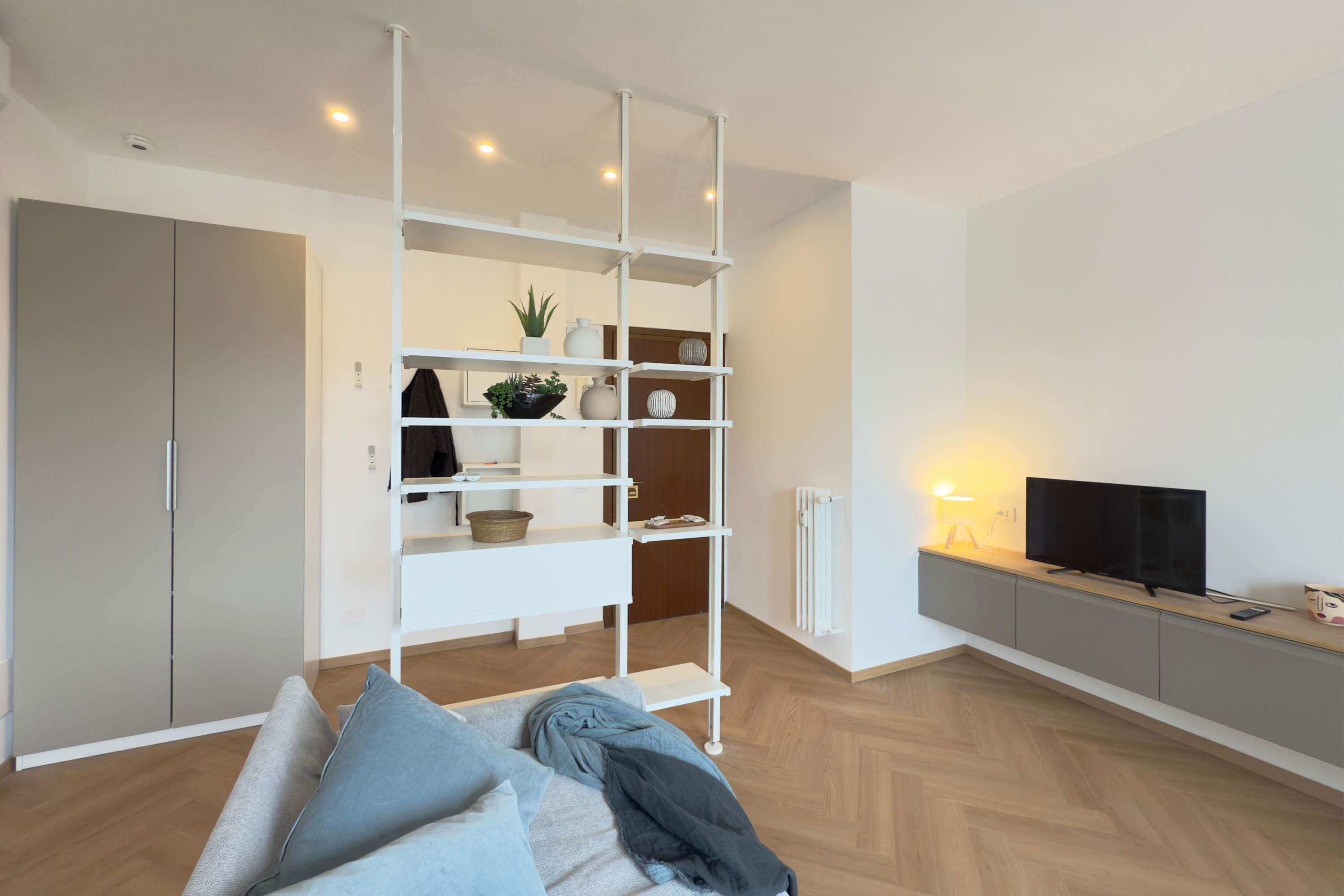 Un salon moderne avec un canapé, une étagère blanche agrémentée d’objets décoratifs, un téléviseur et un radiateur.