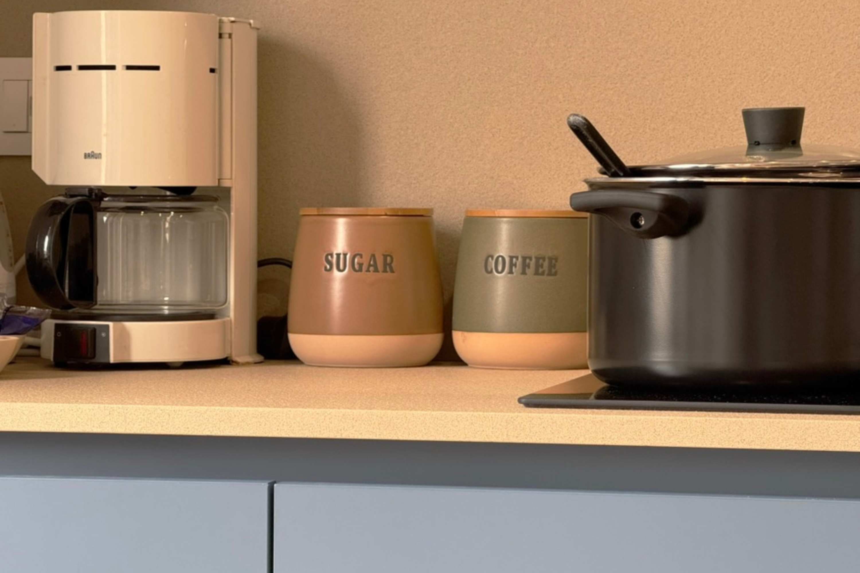 Una encimera de cocina con una cafetera, un tazón de azúcar y un recipiente para café.