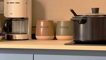 Una encimera de cocina con una cafetera, un tazón de azúcar y un recipiente para café.