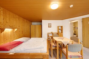 Une pièce aux murs lambrissés, contenant un lit, une table, des chaises et une bibliothèque.