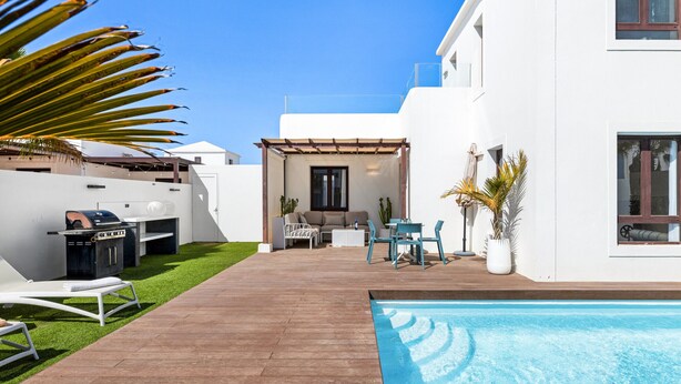Uma área moderna com piscina ao ar livre, deck de madeira, churrasqueira e espaço de estar com cadeiras e uma mesa.