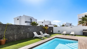 Piscina com espreguiçadeiras brancas e parede de pedra.