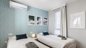 Quarto de hotel com duas camas, ar-condicionado fixado na parede e três quadros emoldurados.