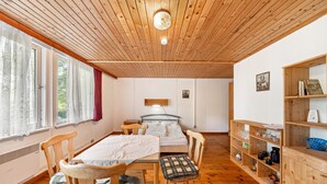 Une pièce avec un plafond en bois, un lit, une table avec des chaises, une bibliothèque et une fenêtre avec des rideaux.